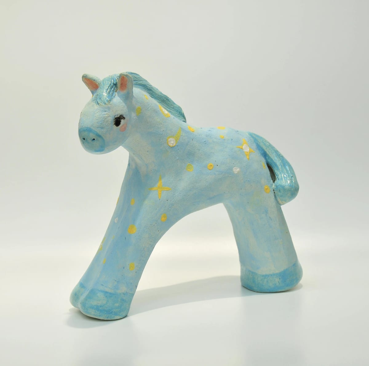 A pale-blue ceramic horse spreads four broad feet, leaving a wide arch beneath its body, with a yellow-and-white star among dots on its side.