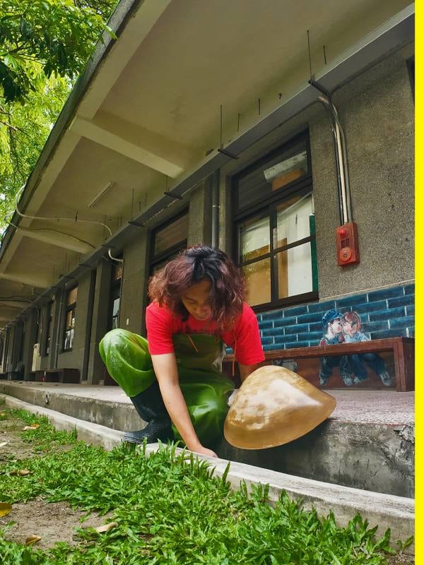 In green waders, Lin Yu-Sheng crouches outside the Banqiao 435 building holding an enlarged clam form almost as broad as his torso.