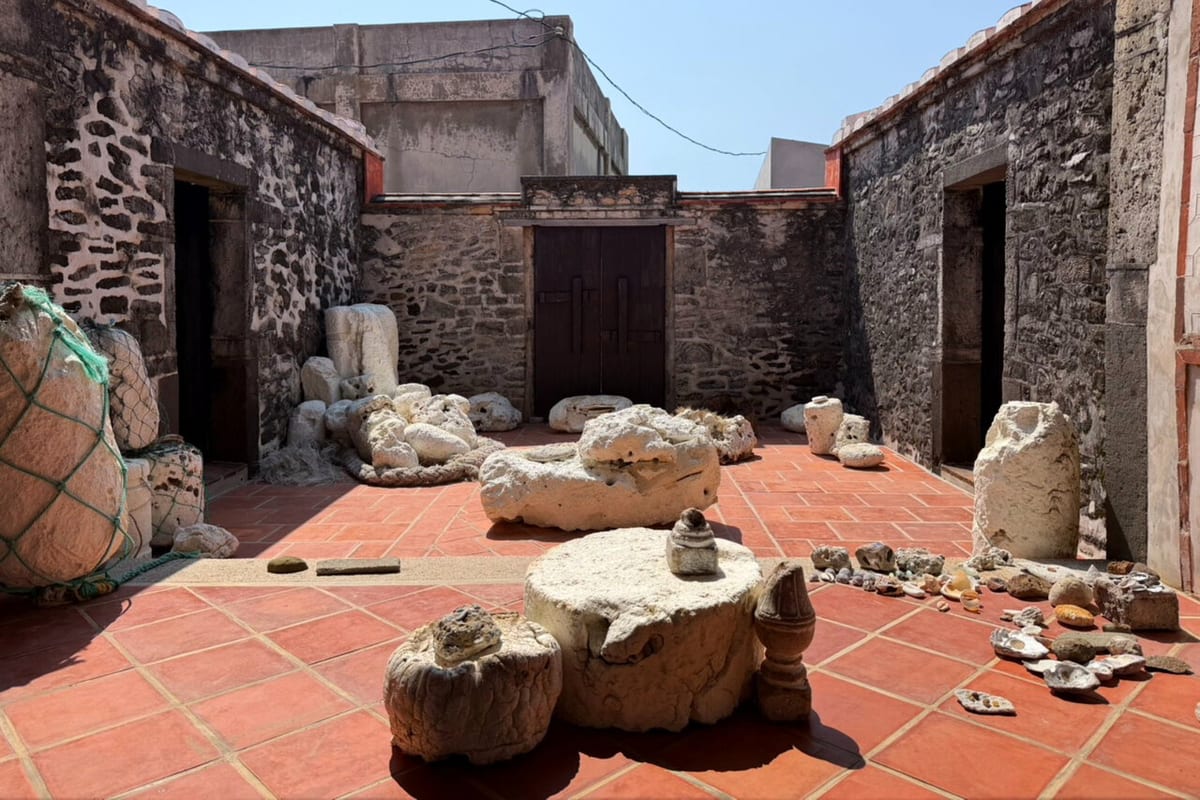 Pale drift material, rope, shells, and small objects are arranged across a sunlit red-tile courtyard in Huazhai.