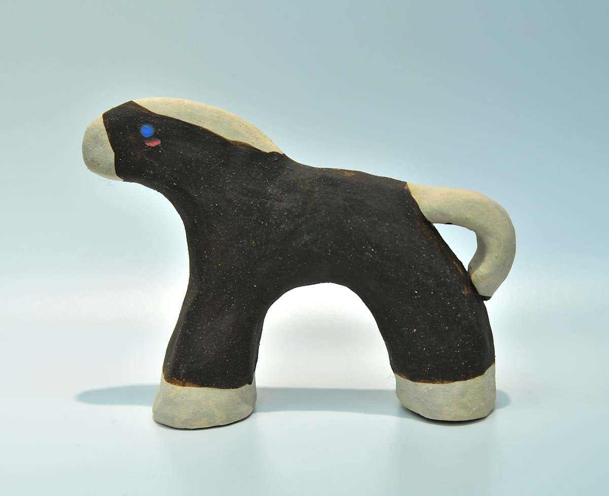 A short-legged ceramic horse stands with a black body, pale muzzle, mane, tail, and hooves, and tiny blue and pink eyes.
