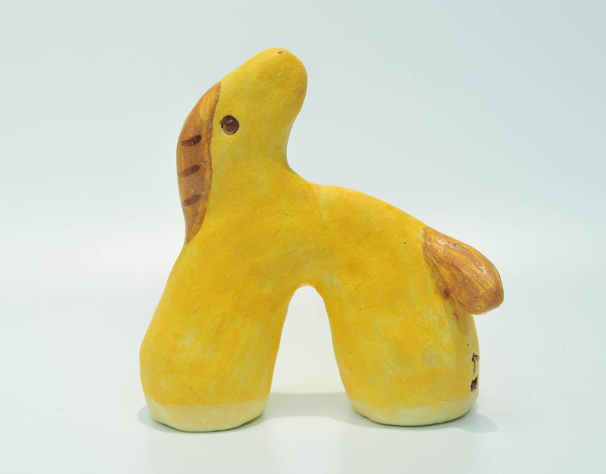 A small mango-yellow ceramic horse lifts its head, with a brown mane and tail painted across the soft yellow surface.