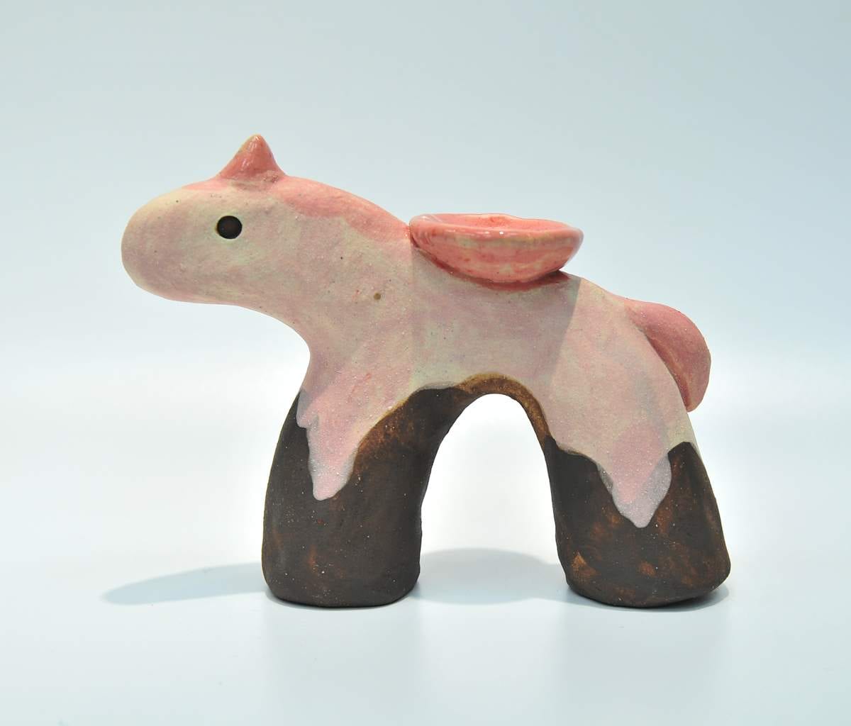 A pale pink ceramic unicorn stands on four dark chocolate-coloured legs with a small pink dish on its back.