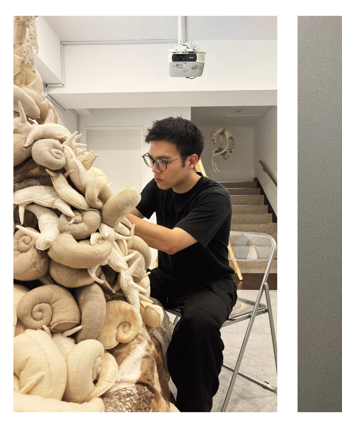 Hou Guan-Ting sits beside the large fiber work, his hands among its repeated pale soft forms.