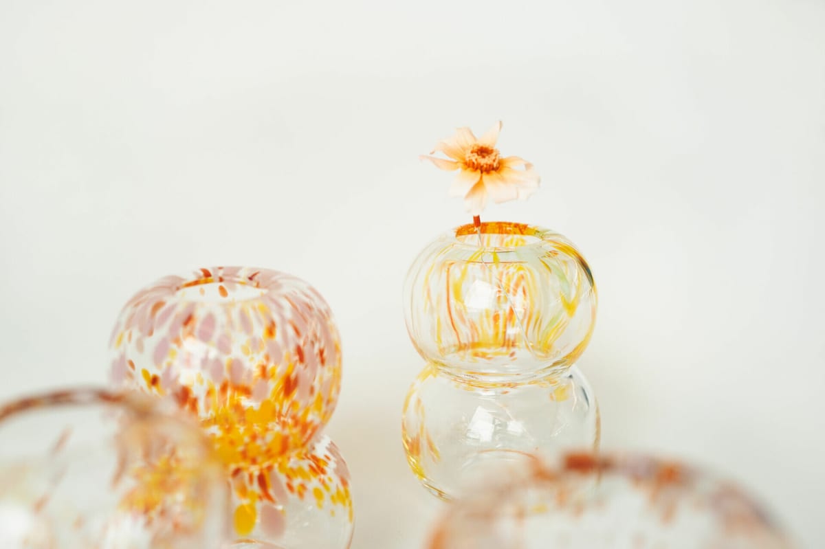 Two glass vessels: one with orange-pink flecks, the other with gold streaks and a single flower.