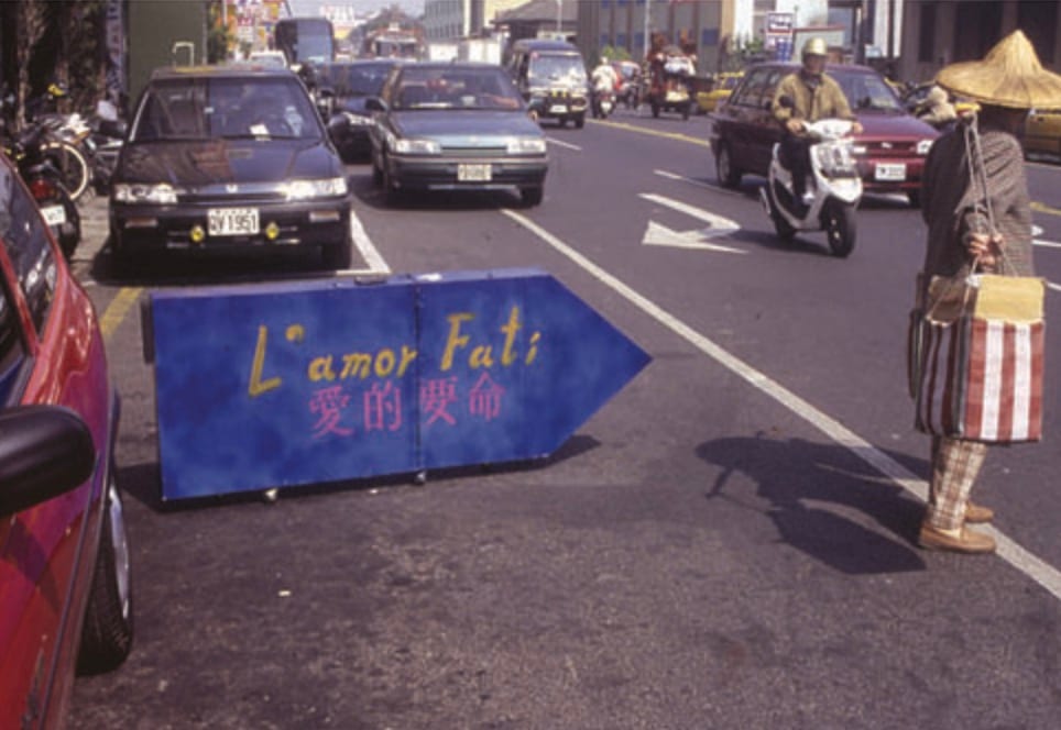 A blue version of the vehicle stands among traffic, with the phrase L'amor Fati 愛的要命 across the frame.