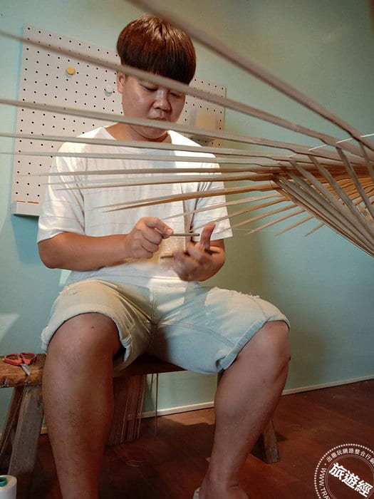 A seated umbrella maker handles long bamboo ribs; the exposed frame stretches across the foreground.