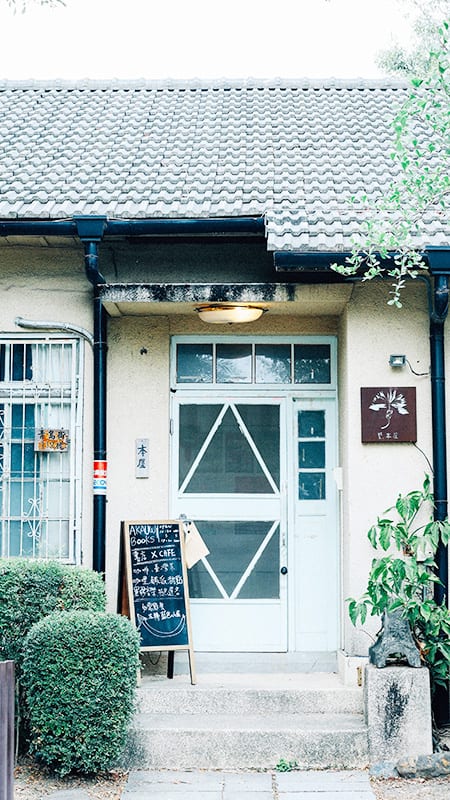 A pale-blue door under a grey tiled roof, beside a small board advertising the bookshop and café.