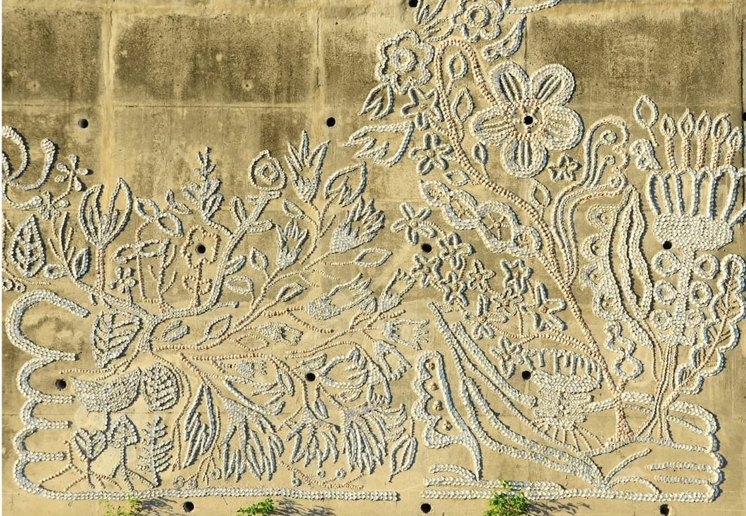 Clam shells form flowers, leaves and curling stems across weathered concrete around dark circular holes.