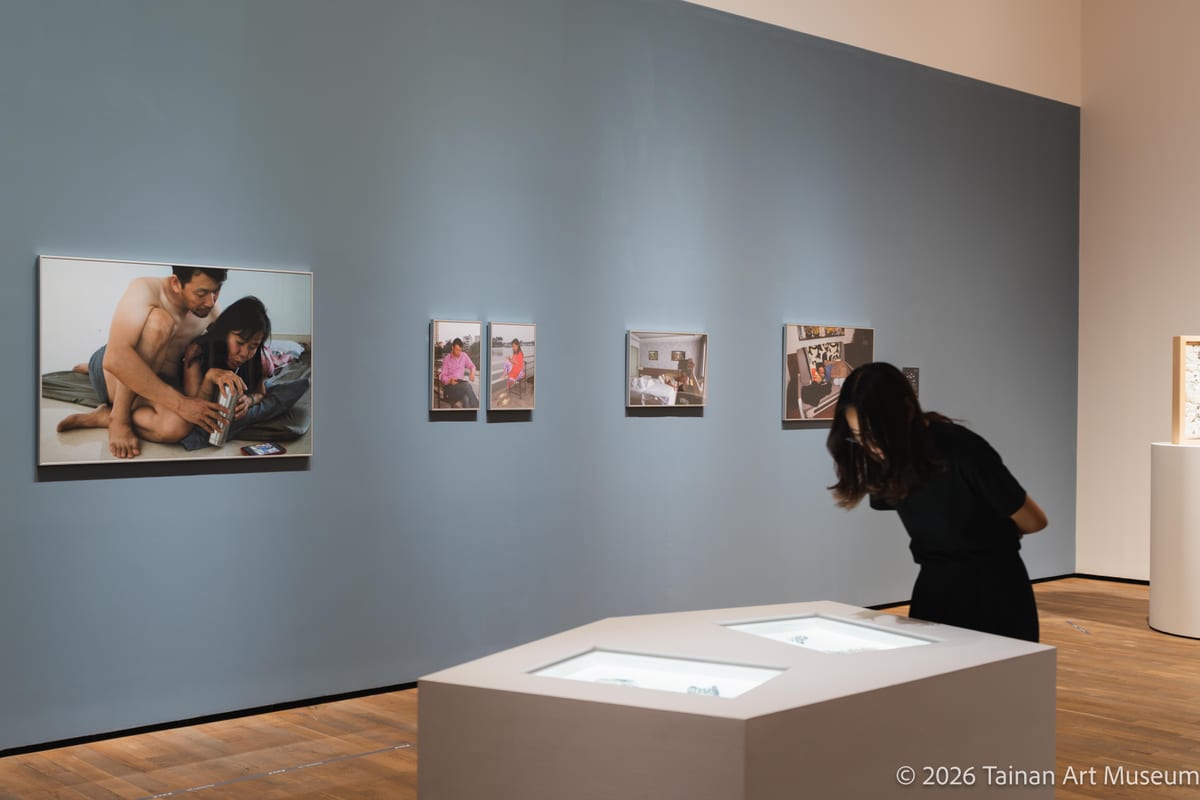 Family photographs stand upright behind illuminated document tables as a visitor bends toward the records.