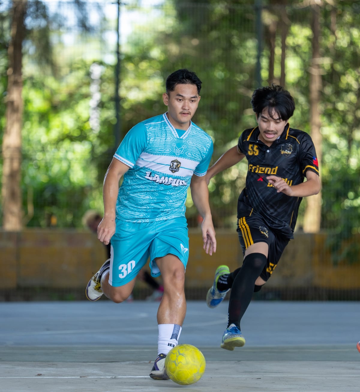 Two footballers in turquoise and black-and-yellow kits concentrate on a yellow ball near the bottom of the frame.