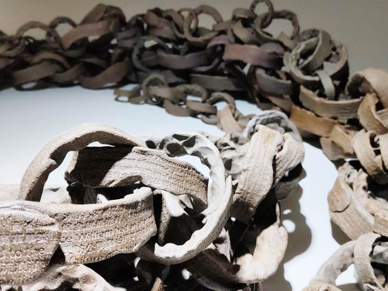 In the foreground, stamped lines of text are legible on rough ceramic chain links; more chains wind across the floor behind.