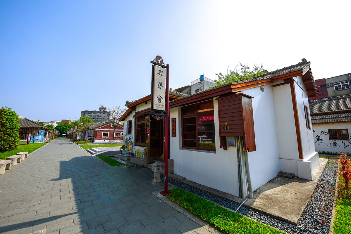 Dark wooden windows, an open timber door and a grey tiled roof on a white-walled house, beside the lane of studios.