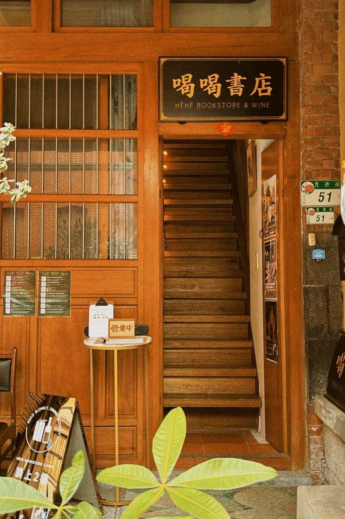 Wooden entrance and staircase under the HĒHĒ Bookstore & Wine sign, with number 51 on the right.