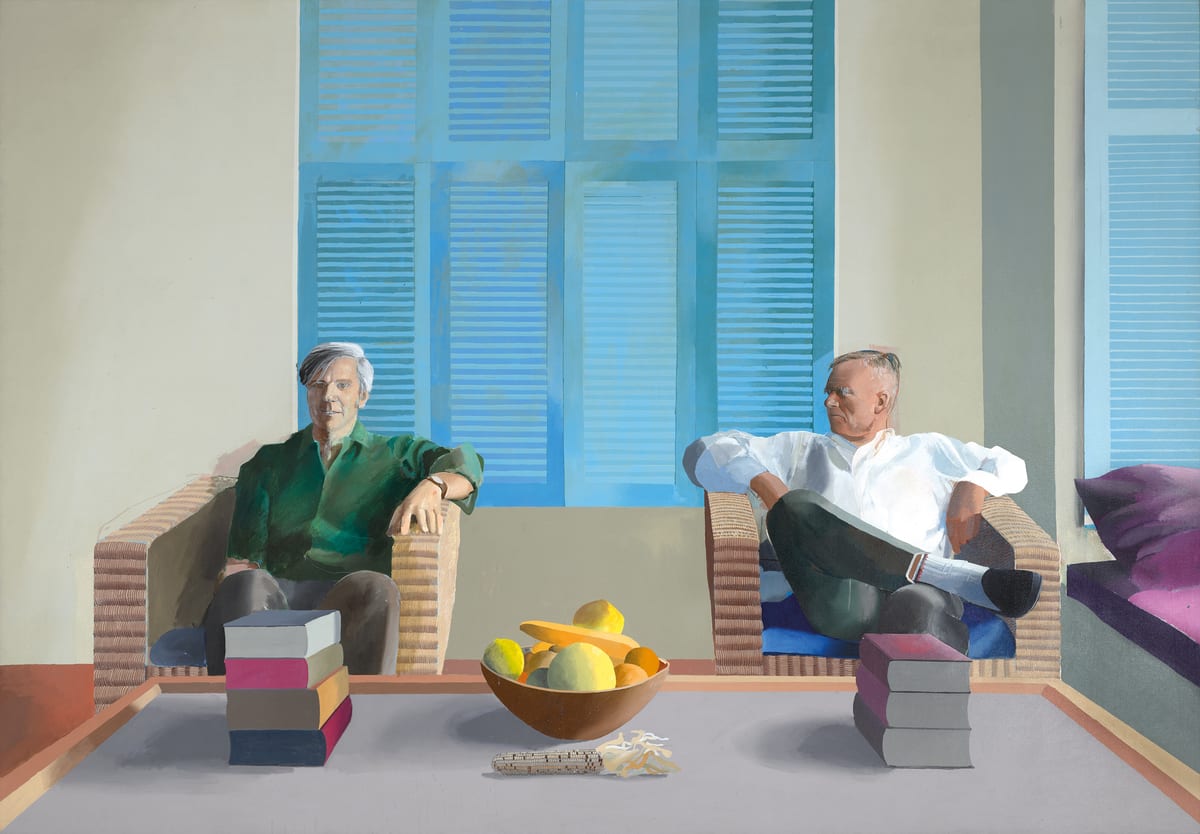 Two men sit in separate wicker chairs, one in a green shirt and the other in white with crossed legs. Blue shutters stand behind them; books and a fruit bowl occupy the foreground table.