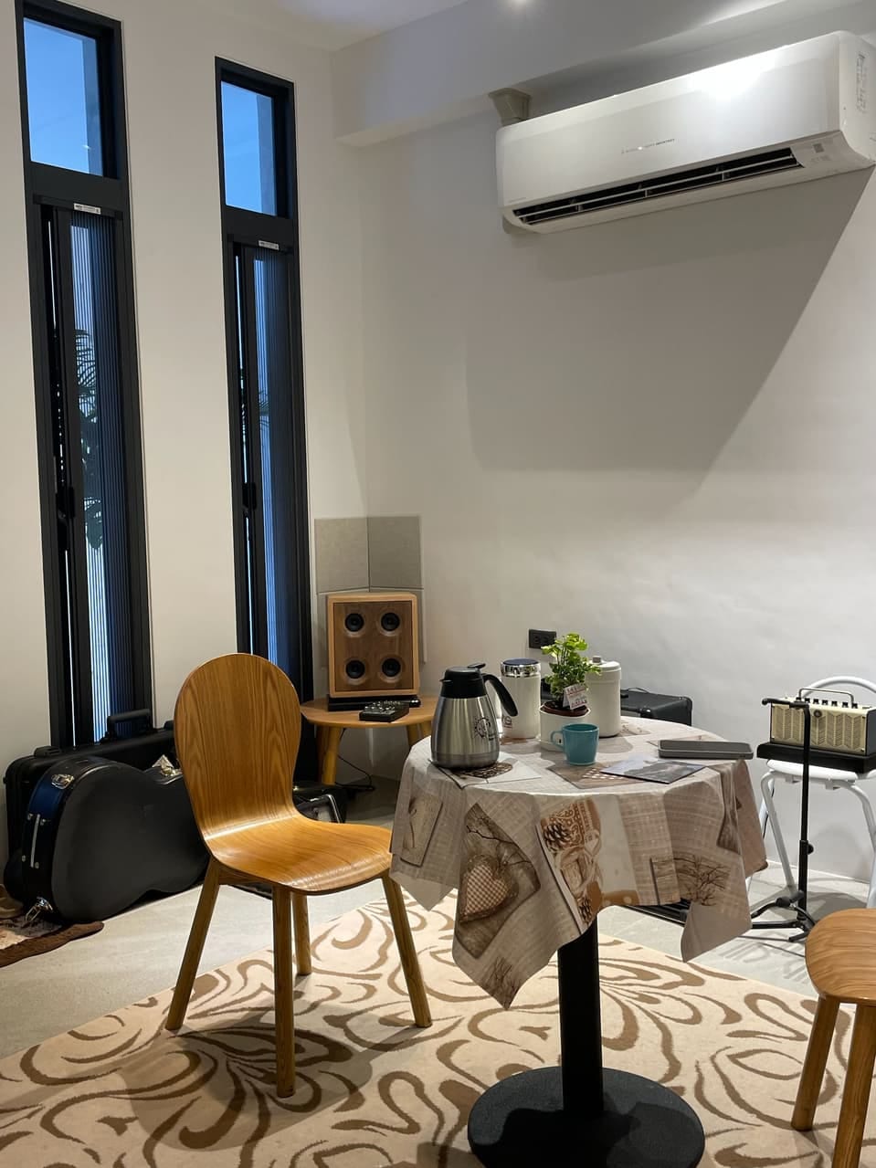 A wooden chair and cloth-covered table beside a four-driver wooden speaker, guitar cases and an amplifier.