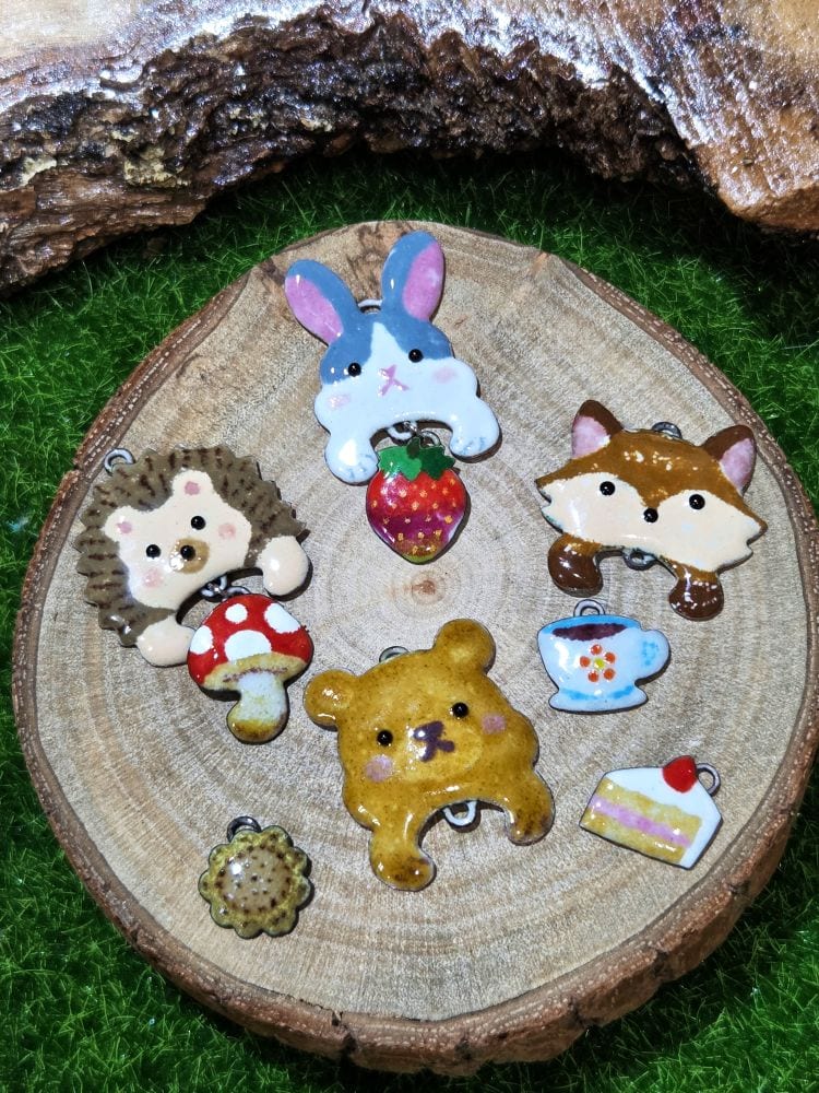 Glossy enamel rabbit, fox, bear and hedgehog charms with a strawberry, cake, teacup and mushroom on a round wooden slice.