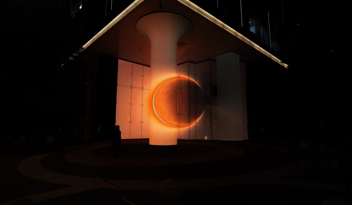 A glowing orange lunar ring crosses a column and the glass walls beneath a dark canopy at night.