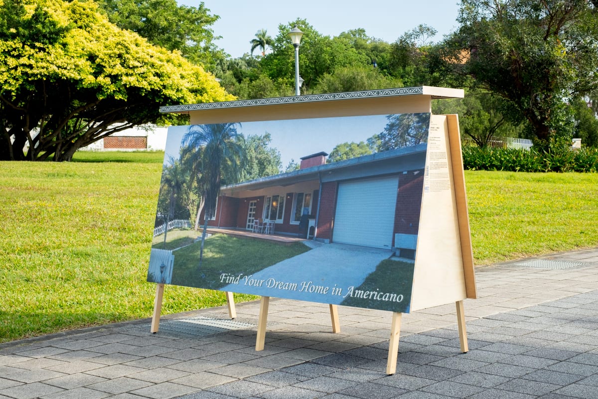 A freestanding photograph beside the park lawn shows a single-storey house, palms, grass and a garage, with the words Find Your Dream Home in Americano.