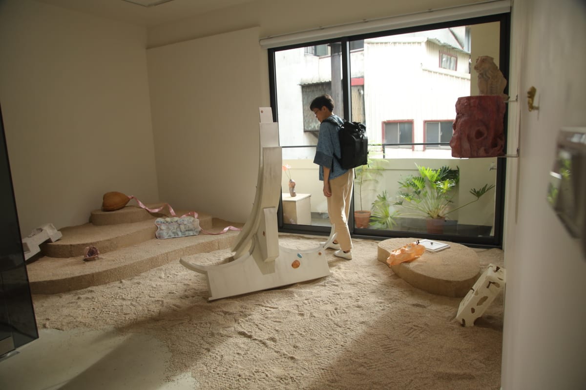Granular brown material covers the gallery floor, with a tall curved white fragment standing near the centre and smaller forms scattered around it.