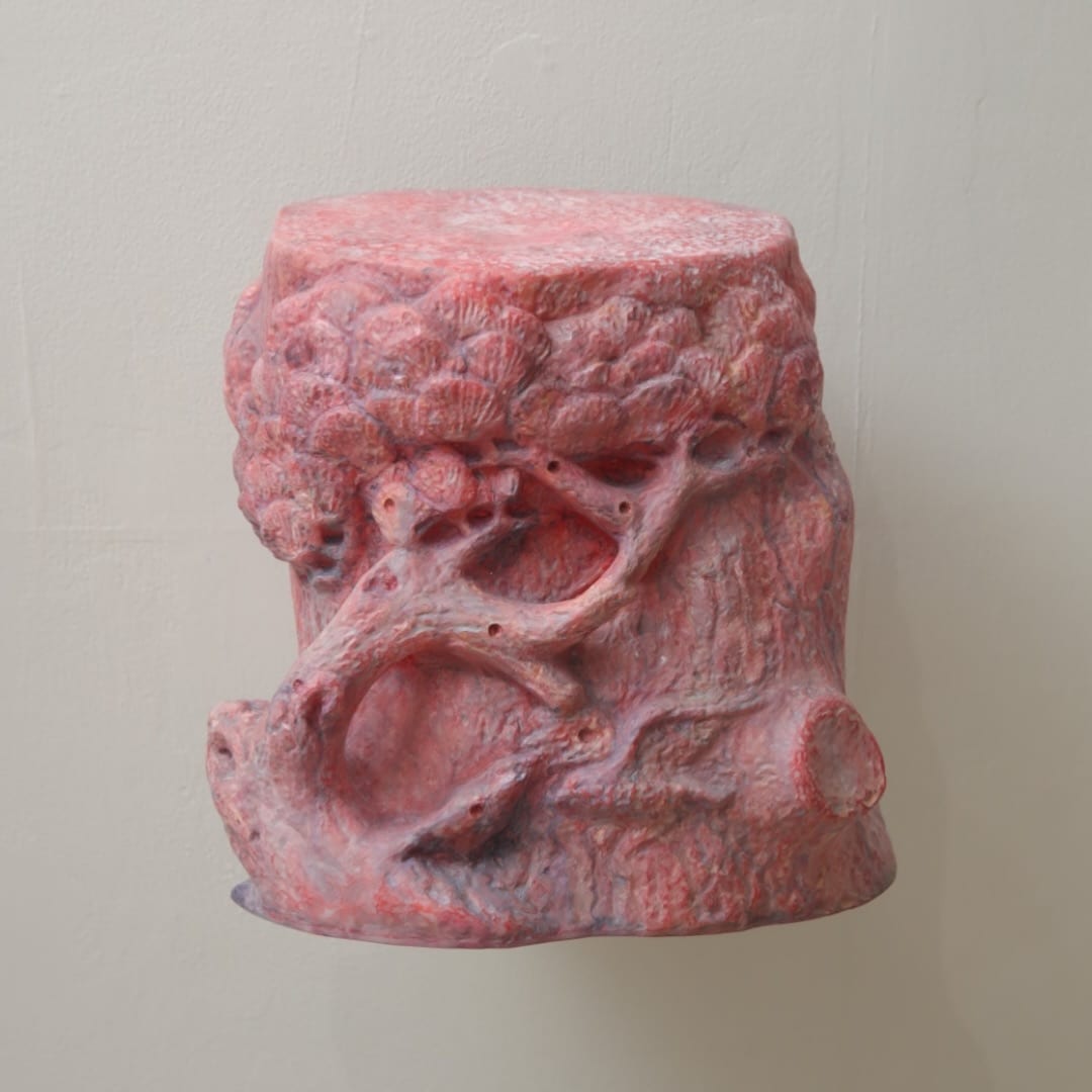 A crimson block of a sculpture with pine trunks, branches and low park relief wrapping around its sides and upper edge.