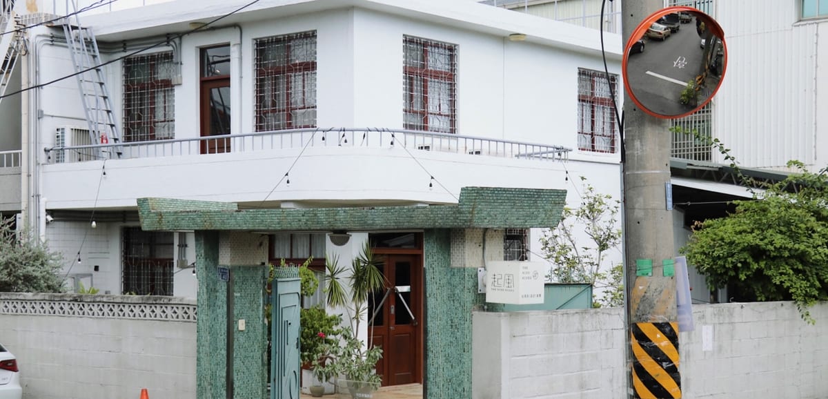 SWAYTEA's white old house with green doors and windows, plants and seats outside.