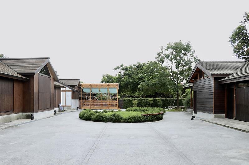 Paths and greenery in the courtyard between the Experimental Wood Workshop's wooden buildings.