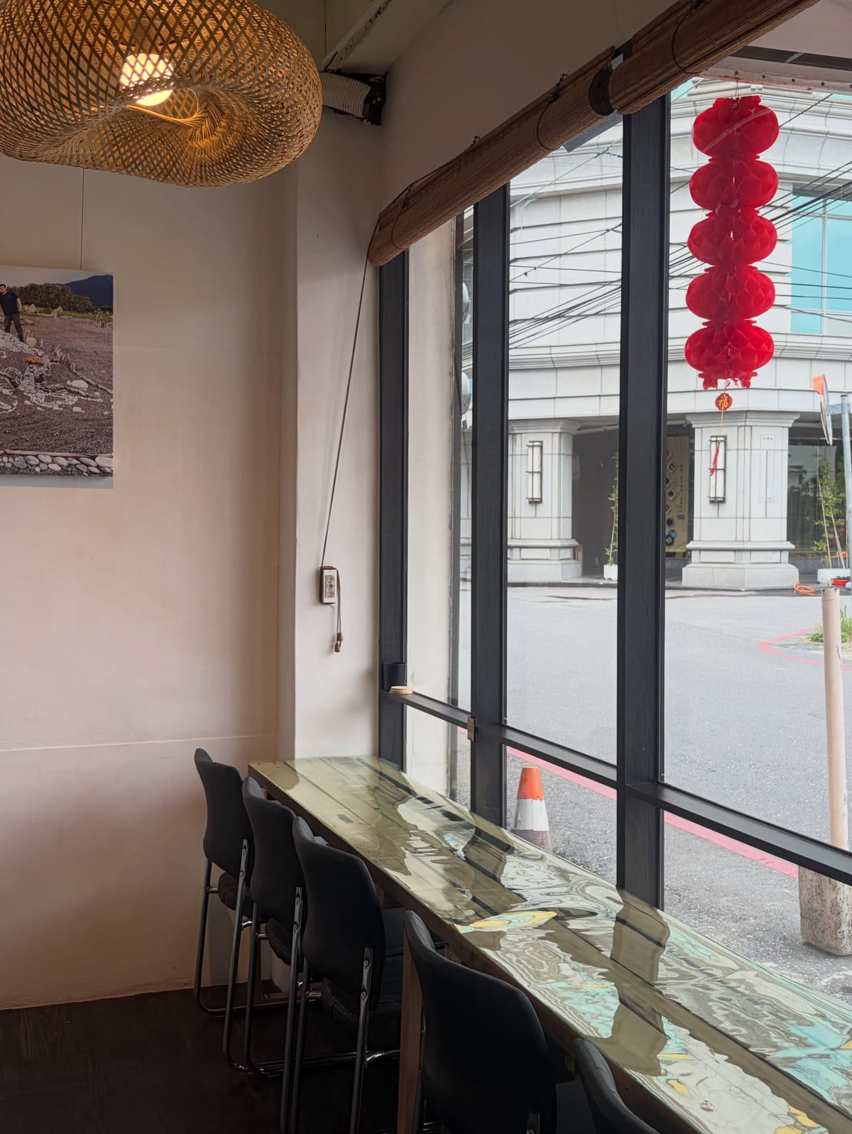 A long counter with seats runs along the street-facing window, under a hanging woven lampshade.