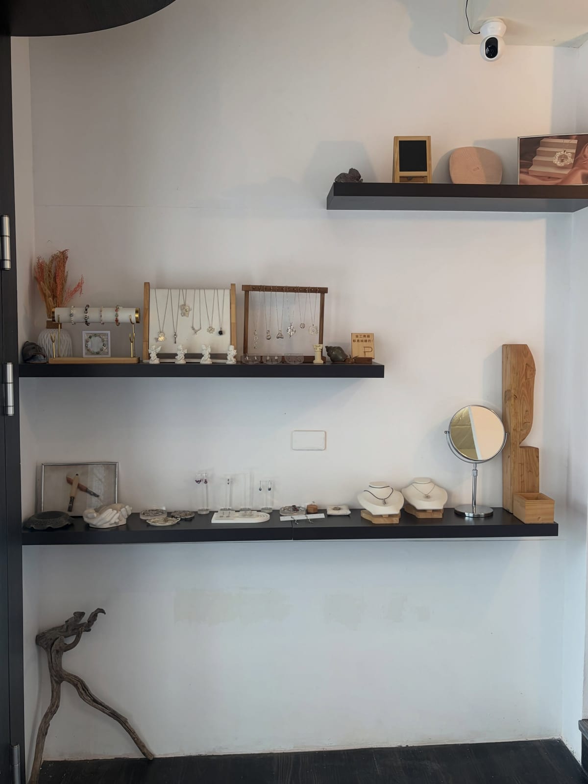 Three dark shelves hold necklaces, small objects and woodwork.
