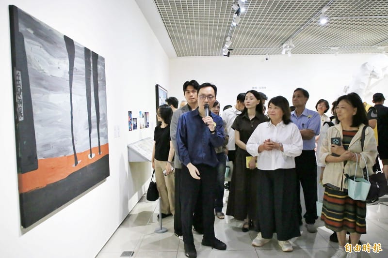 Visitors stand between a large white angular sculpture and a wall of paintings in the gallery on opening day.