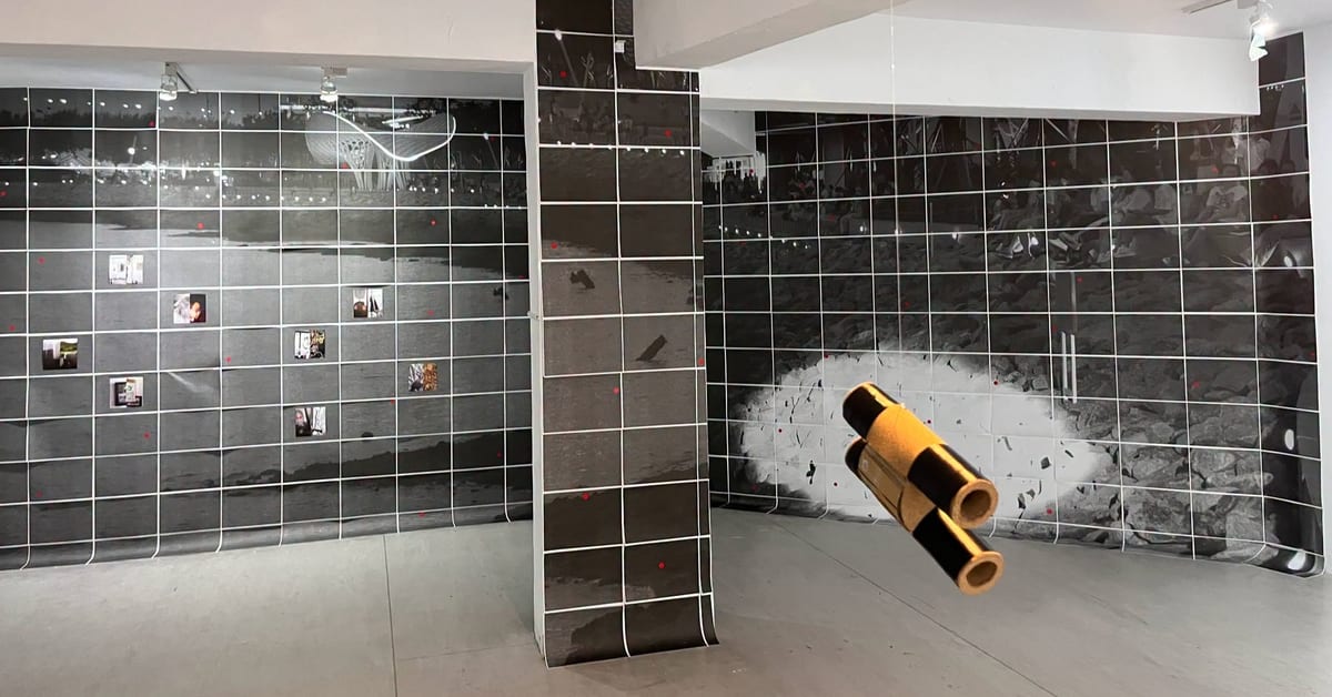 Black-and-white photographic panels with a white grid cover walls and a pillar. Small colour images interrupt them, while yellow binoculars hang in the foreground.