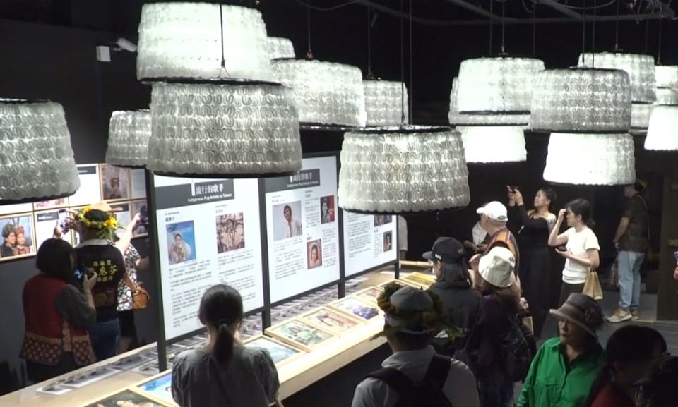 Visitors move between singer-history panels and cases of records and photographs, beneath low hanging lights patterned with Indigenous motifs.