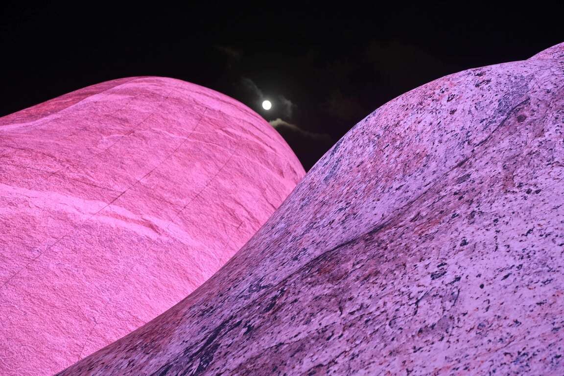 Pink and purple inflatable boulders fill the night photograph, with a small moon between them.