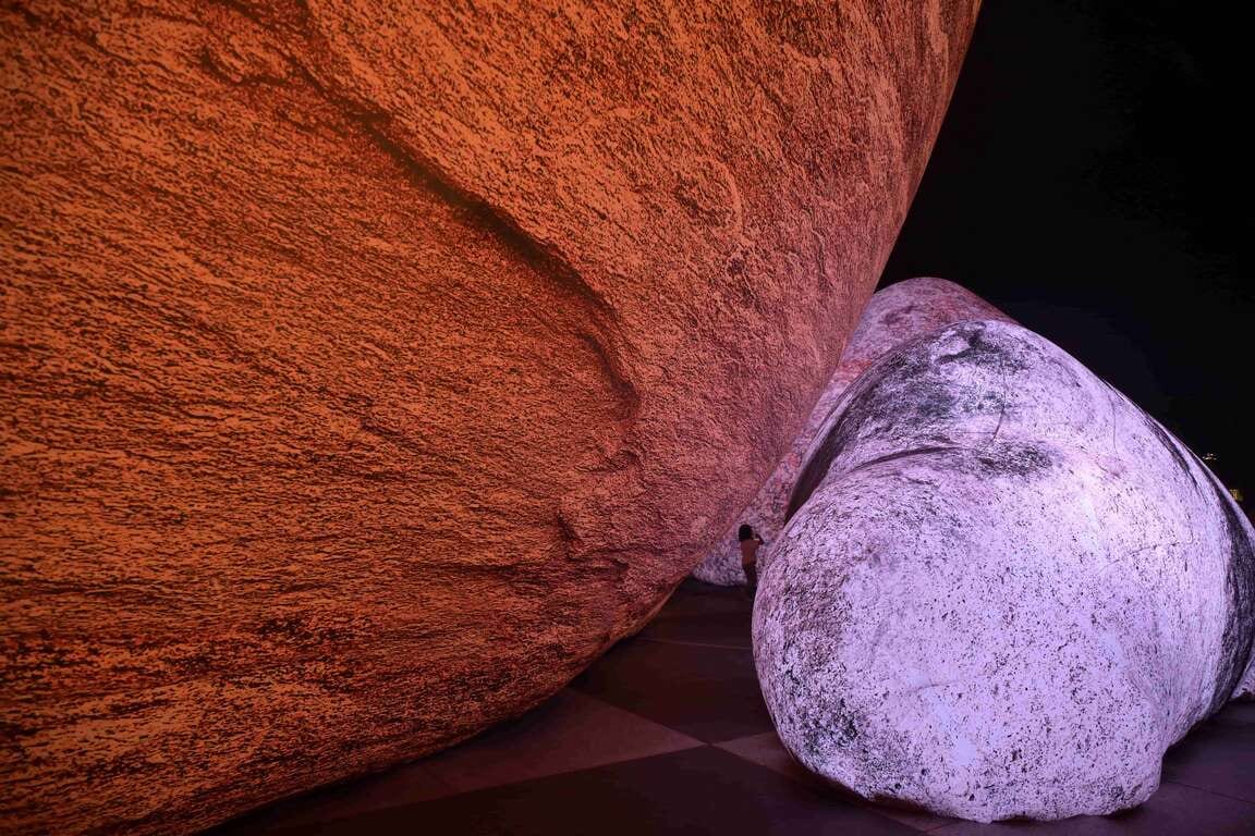 A small figure between orange and purple boulders at the Sunrise Boulevard night installation.