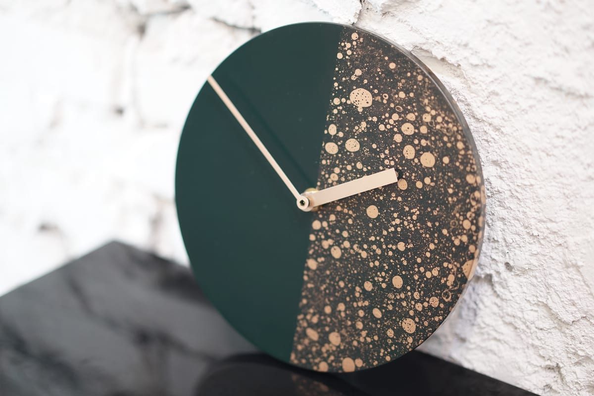 A dark blue clock with gold-coloured circular patterns on its right half, photographed against a white brick wall.