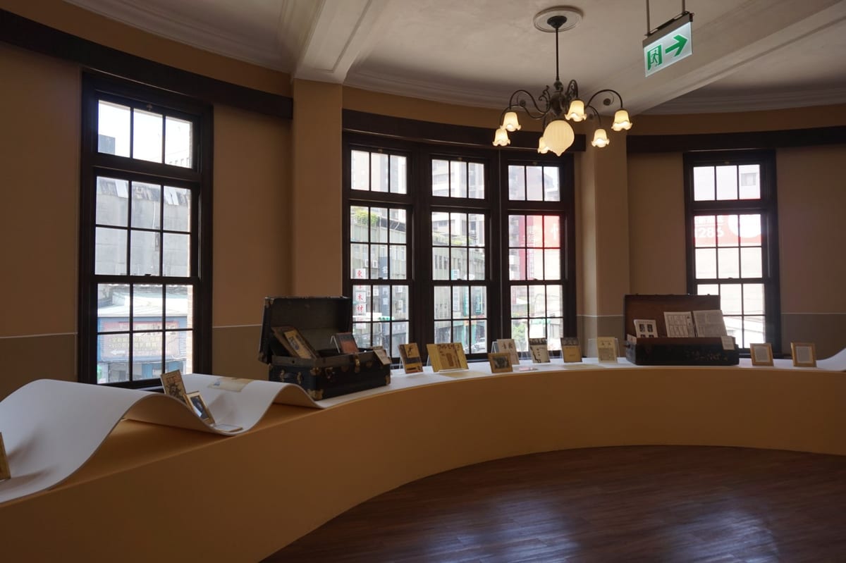 A gallery inside the former police station: a curved wooden display table encircles the room beneath arched windows and a hanging lamp.