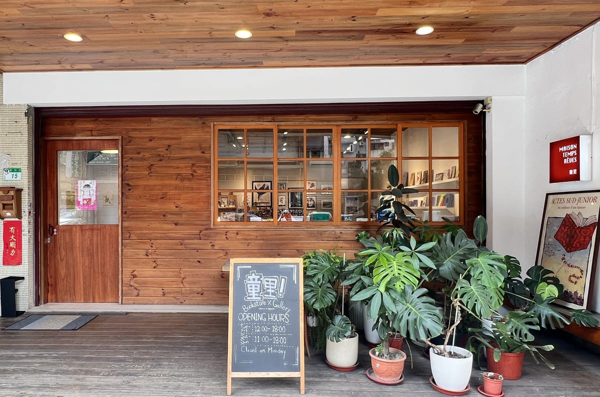 A wooden shopfront with picture books behind the glass, potted plants and a small blackboard outside.