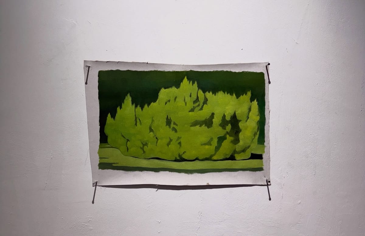 Lime-green tree shapes against a deep-green ground, with dark gaps within the foliage. A pale uneven border surrounds the work, pinned at four corners on a white gallery wall.