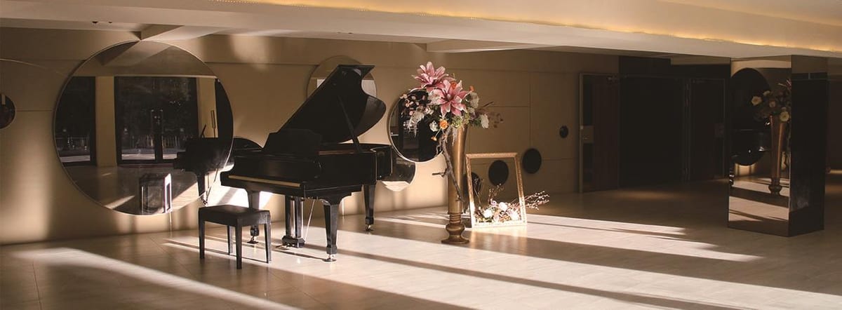 A grand piano in the sunlit room at Xu Shi Music Library, with circular mirrors and flowers.