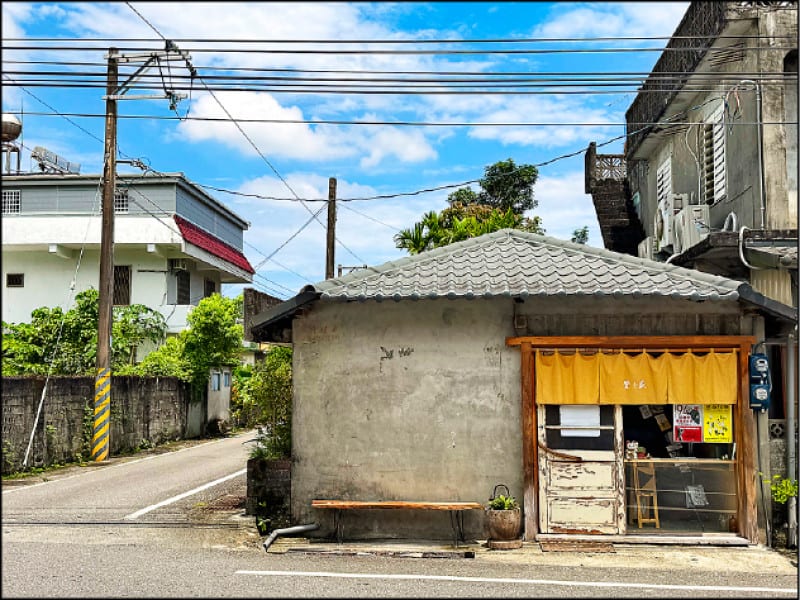 A low gray former warehouse beside Zhongshan Road, an ochre curtain over its entrance, with mountains rising beyond the roofs and power lines.