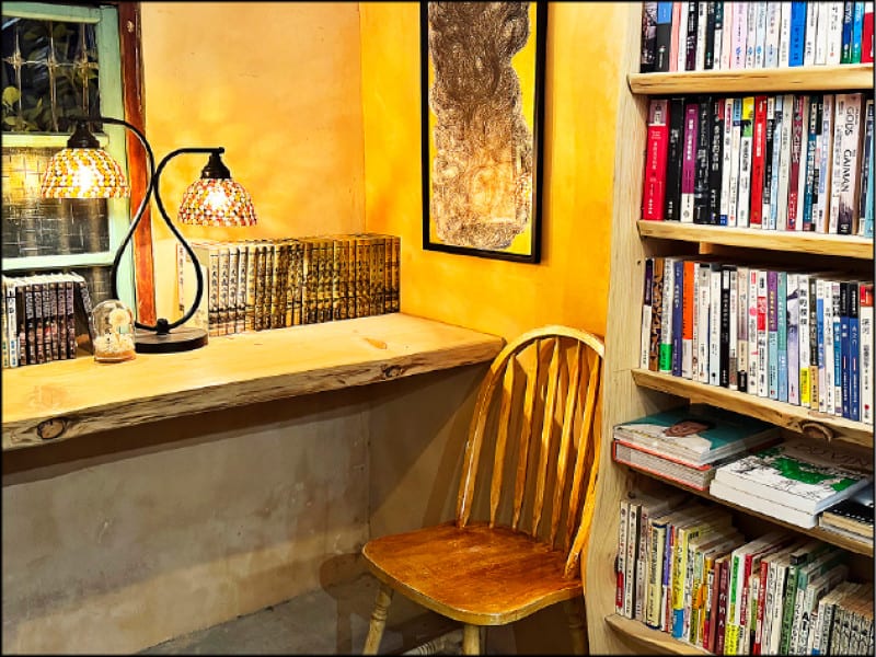 The room's single upholstered chair between a broad wooden table and a wall of books, lit by two mosaic lamps.
