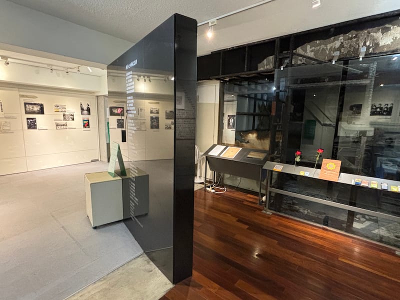 A black wall inside the museum carrying poems, leading to the fire-damaged editor-in-chief's room behind glass.