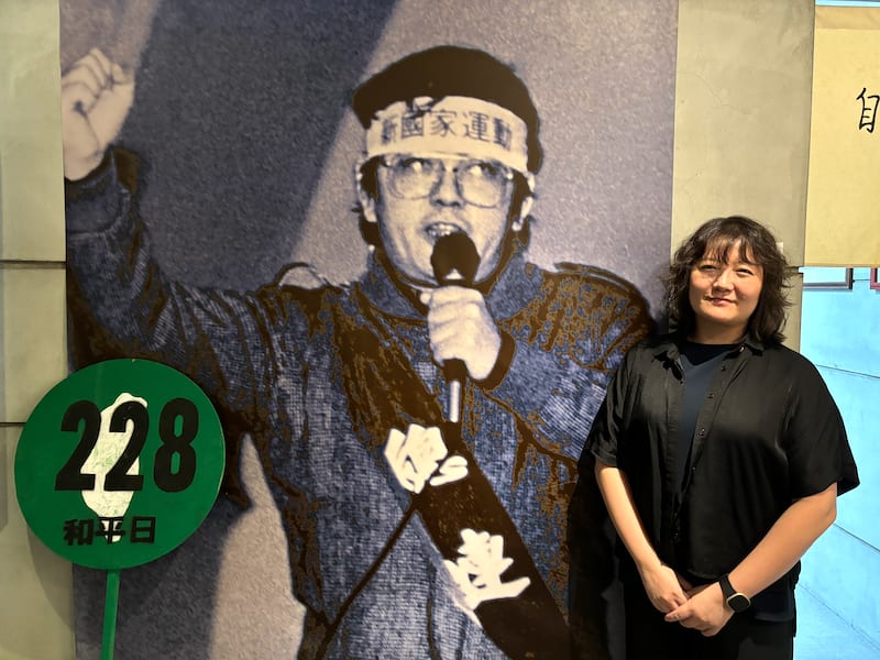 Cheng Chu-mei standing in the museum beside a photograph of her father speaking.