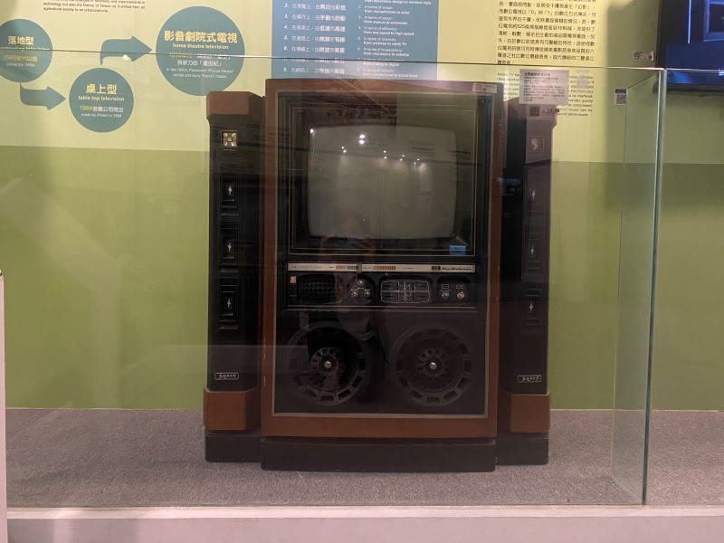 A wood-coloured Tatung Venus television behind glass, with tall side columns and two circular grilles below its screen.