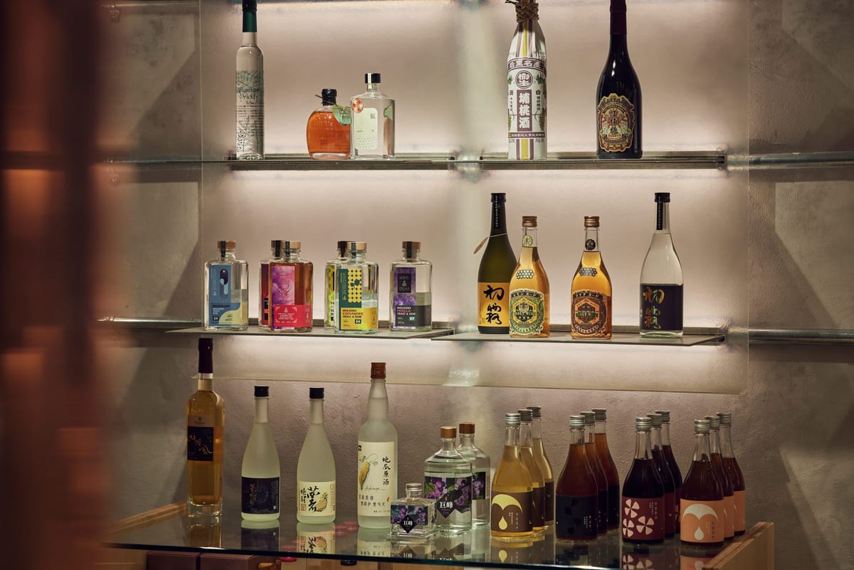 Taiwanese bottles on illuminated glass shelves, tall and square, with labels including sweet potato, grape and honey.