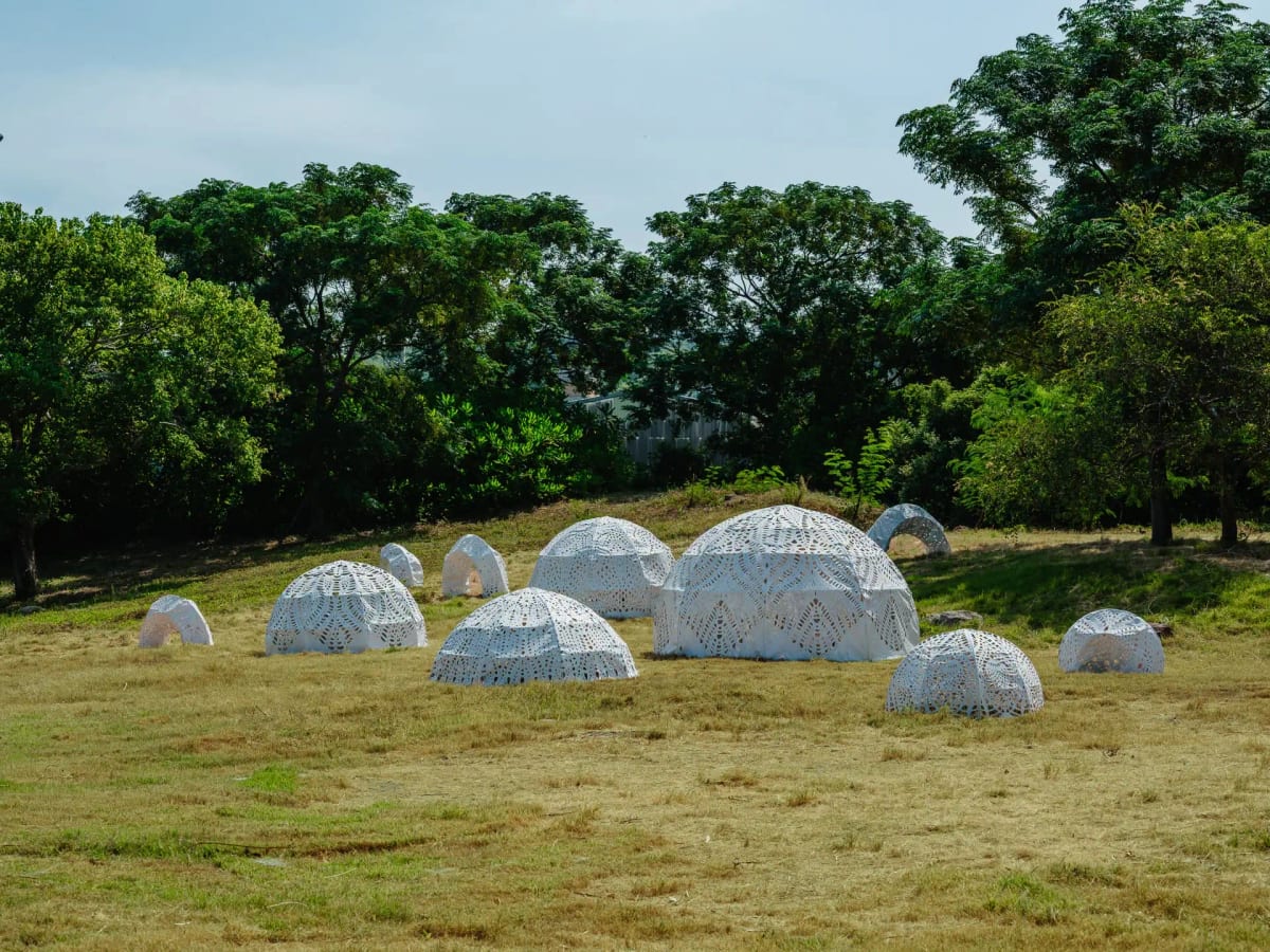 White perforated shell-like arches of different sizes sit on grass beneath trees.