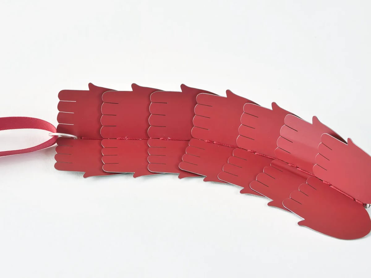 Red hand-shaped metal plates overlap and are joined along their centre by red cord and a silver-coloured ring.