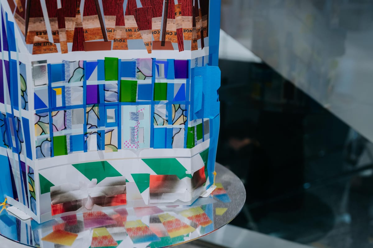 Blue, green and purple translucent pieces and paper sit inside a white grid that turns into a three-dimensional frame.