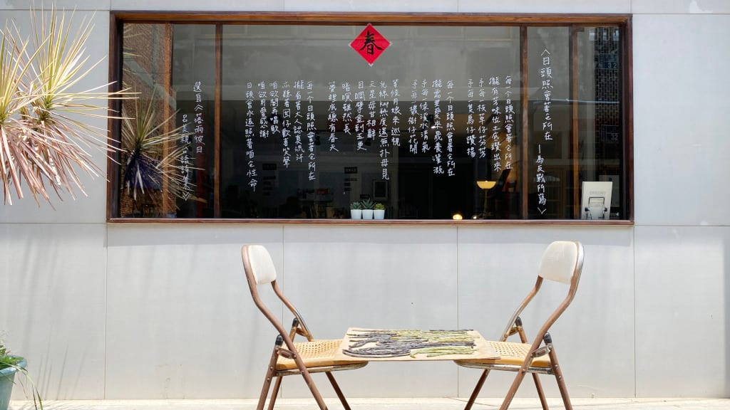 Two wooden chairs face each other across a small table outside the bookstore's window, covered in white Chinese poetry and a red spring decoration.